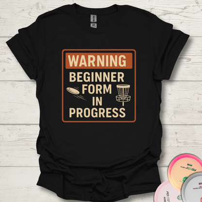 Warning Beginner Form In Progress funny disc golf t-shirt. Unisex funny beginner disc golf shirt on wooden background.