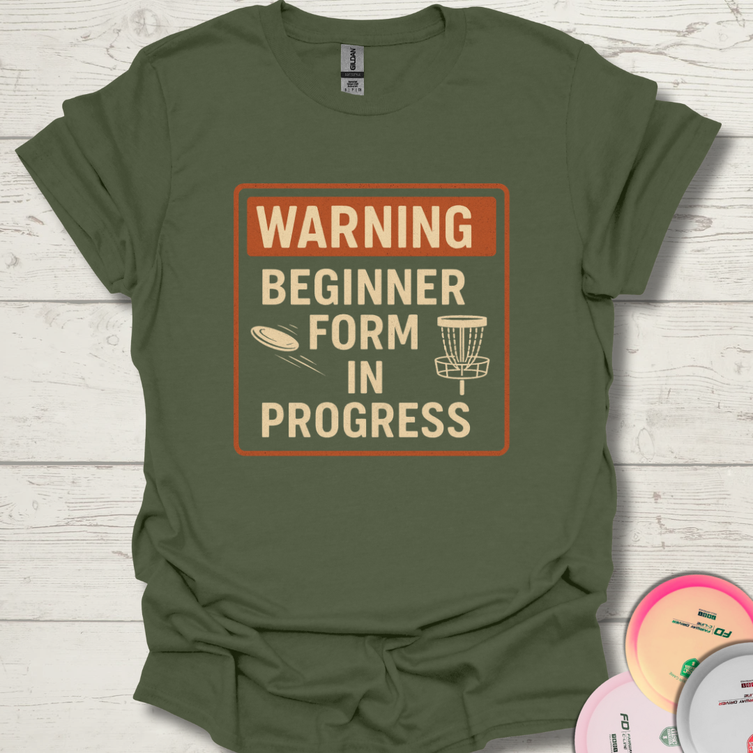 Beginner disc golfer wearing Warning Beginner Form In Progress t-shirt. Funny frisbee golf shirt for beginners. Funny disc golf quote for new players.