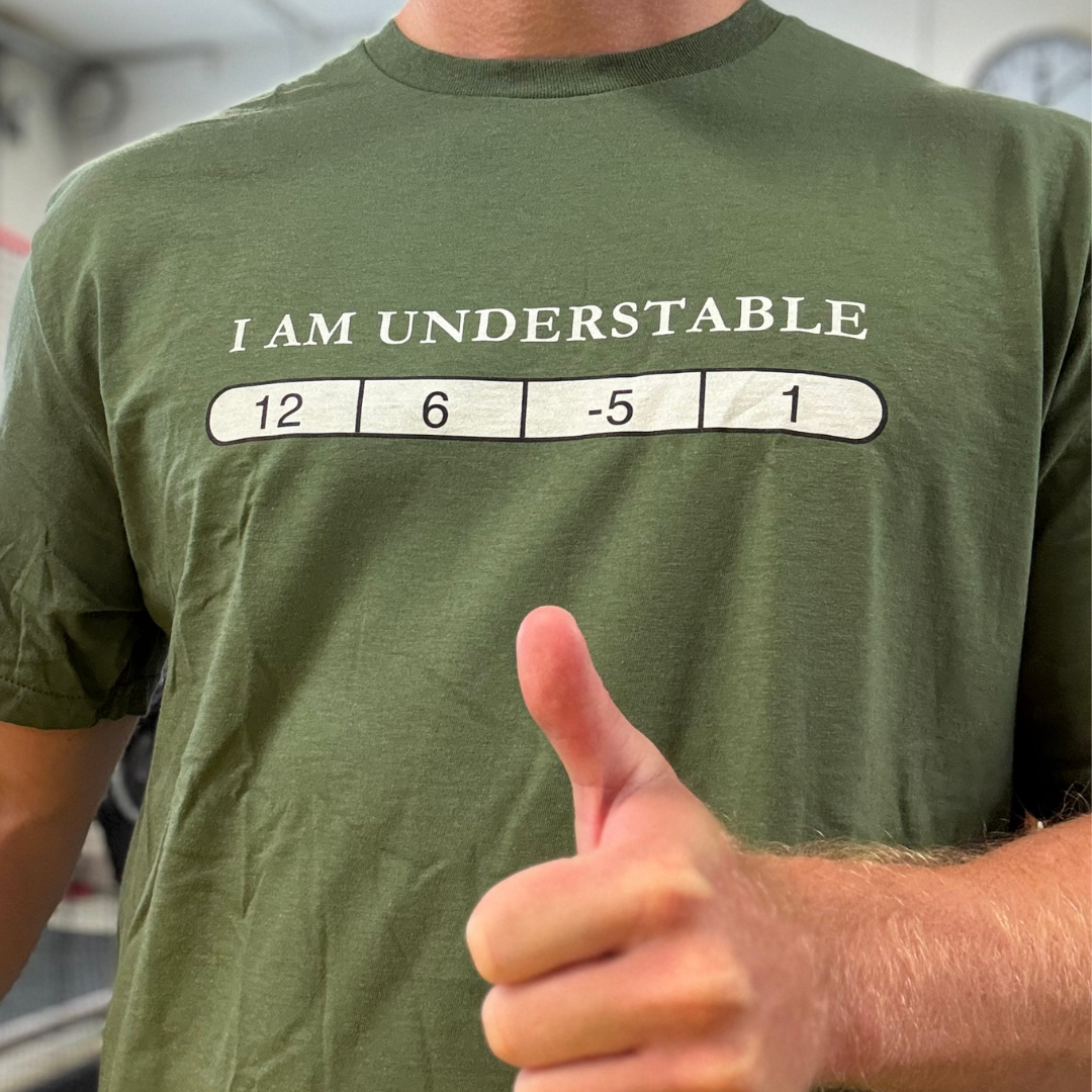 Disc golfer wearing green I Am Understable disc golf shirt giving thumbs up. Man in I Am Understable flight numbers t-shirt with 12 6 -5 1 graphic. Understable disc golf shirt in green with 12 6 -5 1 flight numbers on player. Model wearing I Am Understable disc golf shirt showing flight numbers bar.